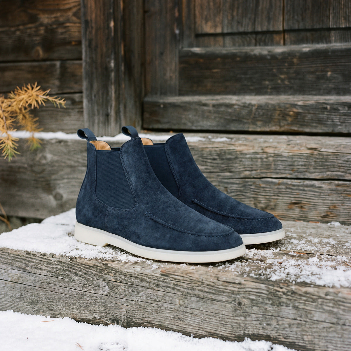 A pair of navy suede Chelsea boots on a snowy timber doorstep