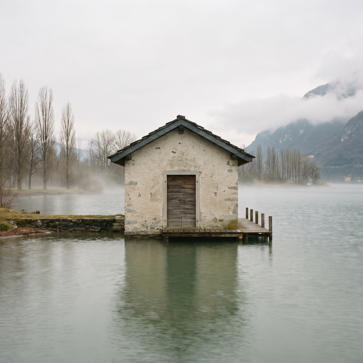 A pale stone boathouse on a still lake at dawn